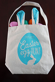 Bunny Bag A canvas tote bag that says Saint Louis University Easter Egg Hunt with an image of an egg surrounding the words and an outline of a bunny underneath. Easter eggs can be seen spilling out of the top of the bag.