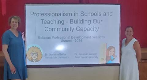 Jeannine Butler, Ed.D., and Jessica Leonard, Ph.D., presenting a Belizean Professional Development Session Two professors stand on either side of a video screen that reads "Professionalism in Schools and Teaching: Building Our Community Capacity. Belizean Professional Development Sessions June 2024"